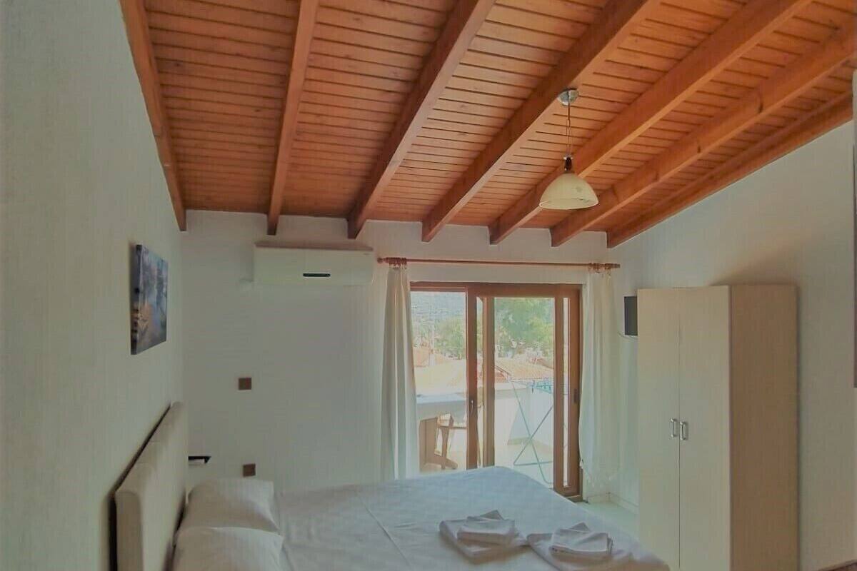 A bedroom with a wooden ceiling, a bed, a wardrobe, and a window with a view of the outside.