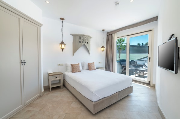 Une chambre dotée d’un grand lit, d’une table de chevet, d’une armoire, d’une télévision et d’un balcon aménagé avec du mobilier d’extérieur.