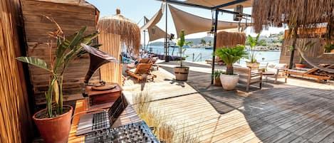 Terraza de madera con sillones de descanso y sombrillas, con vista a un cuerpo de agua.