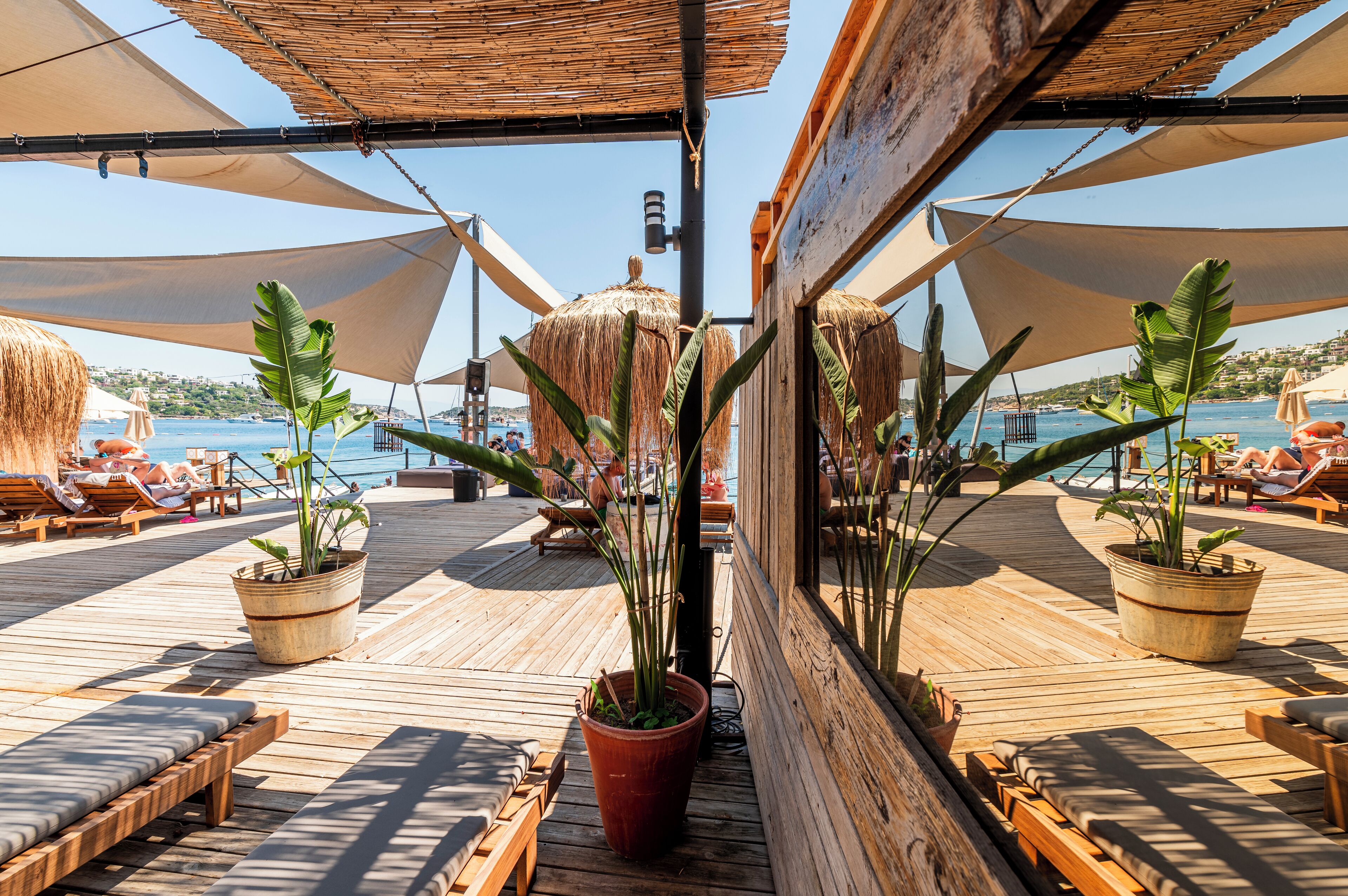 A wooden deck with lounge chairs and potted plants, overlooking a body of water.