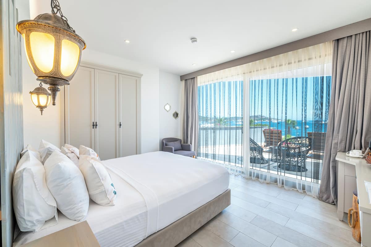 A hotel room with a large bed, a balcony with outdoor furniture, and a view of the sea.