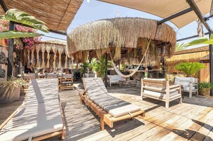 A wooden deck with lounge chairs, a hammock, and a thatched-roof structure.
