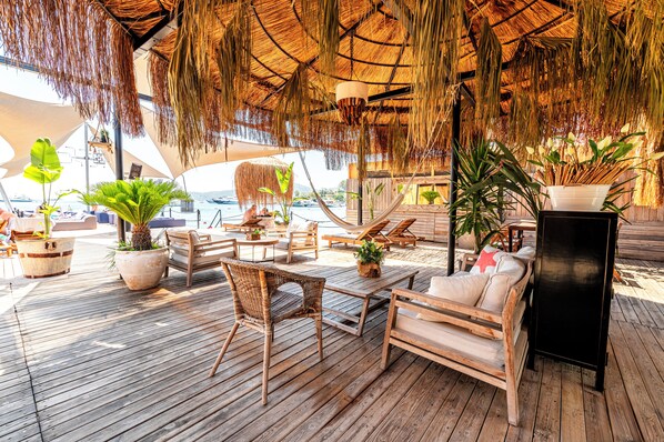 A wooden deck with lounge chairs and tables, surrounded by potted plants and a thatched roof. - Elista Hotel & Spa (Bodrum)
