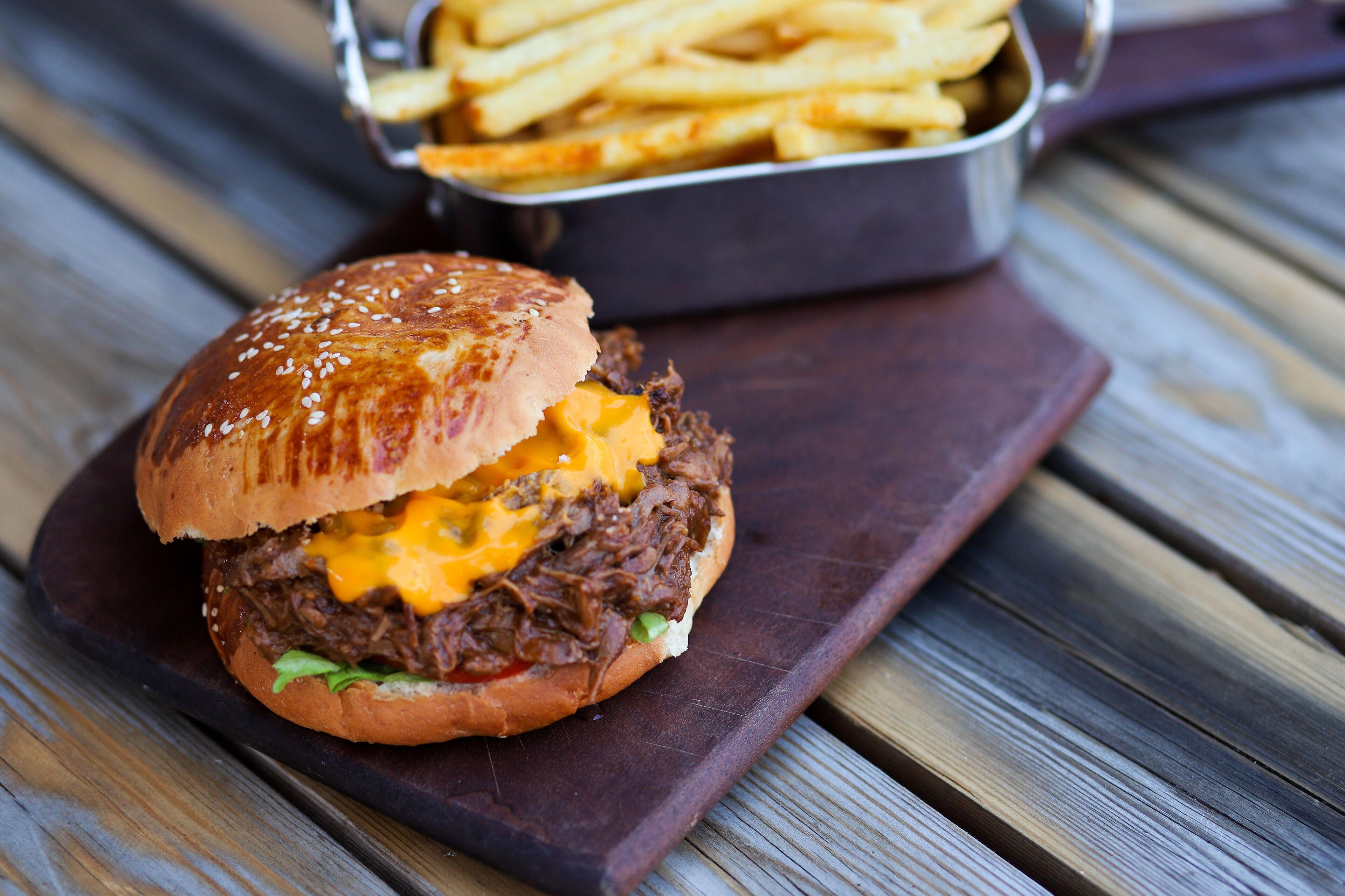A pulled pork sandwich on a sesame seed bun with melted cheese, accompanied by a side of French fries.