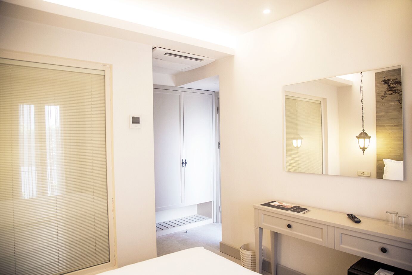 A hotel room with a large mirror, a bedside table with a lamp, and a wardrobe.