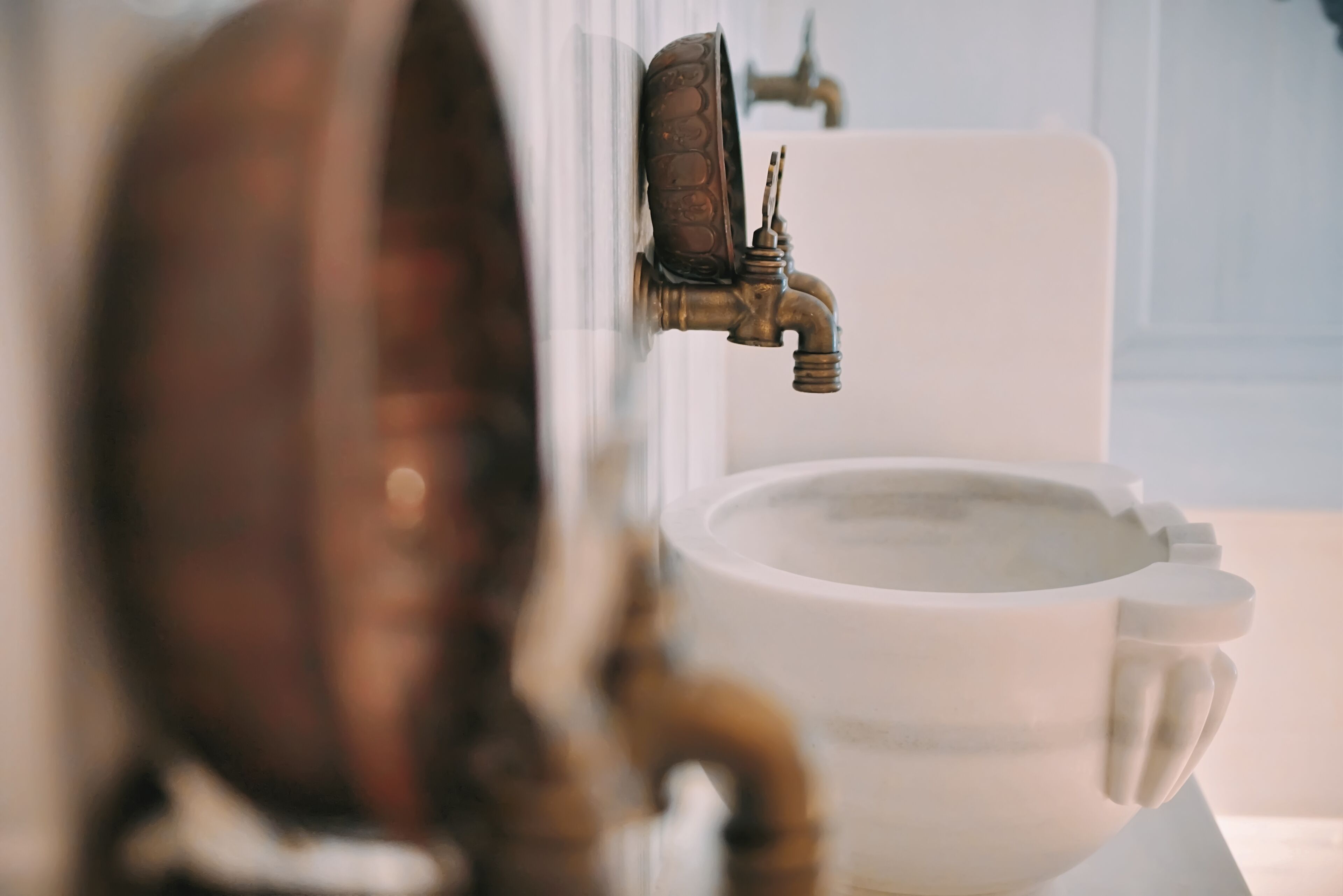 Un baño con un lavamanos blanco, un grifo de latón y un espejo.