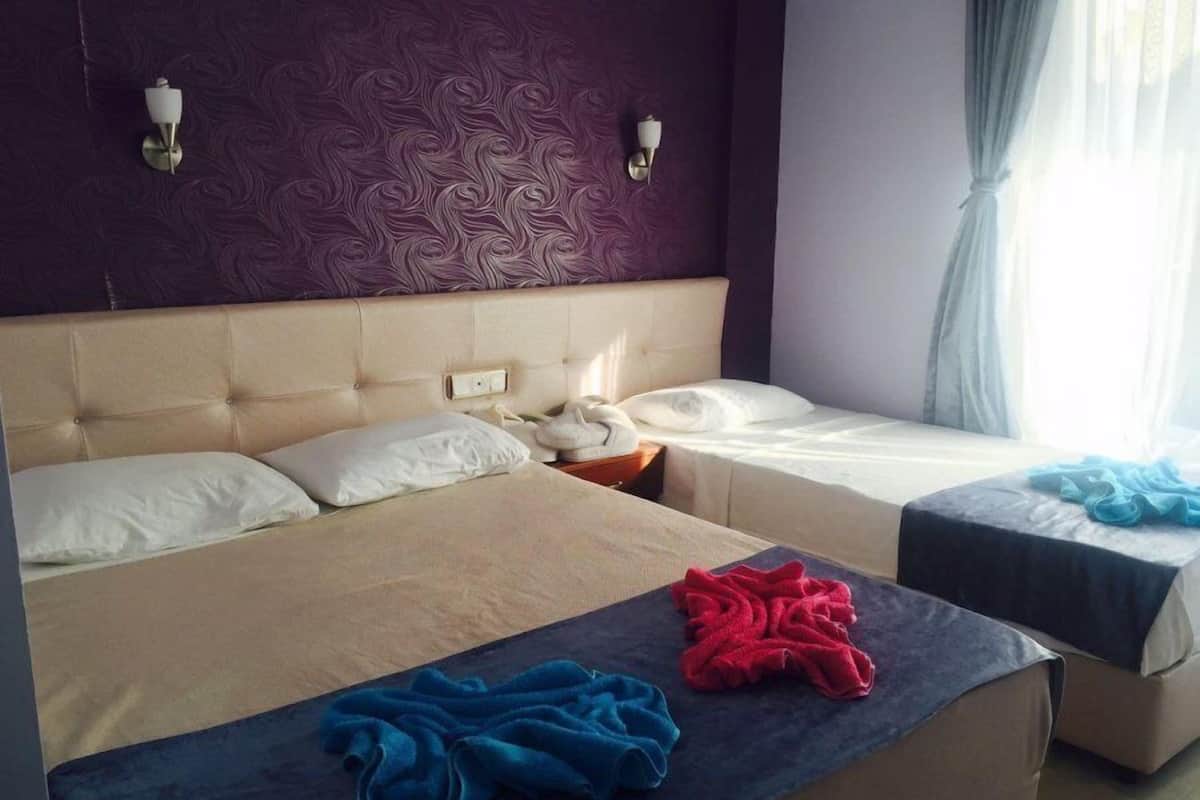 Habitación de hotel con dos camas, una pared texturizada color púrpura y una ventana con cortinas claras.