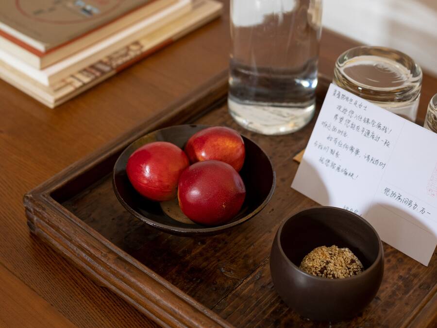 Een houten dienblad met een fles, een schaal rode vruchten en een schaal bruine substantie, plus een kaartje.