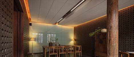 A dining area with a wooden table and chairs, a cabinet with a plant, and a patterned wall.