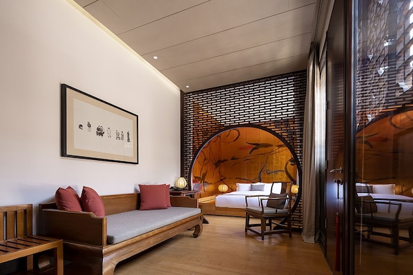 A modern hotel room with a wooden floor, a sofa with red cushions, a bed with white linens, and a wall with a wooden lattice design. - Jing's Residence (Jinzhong)