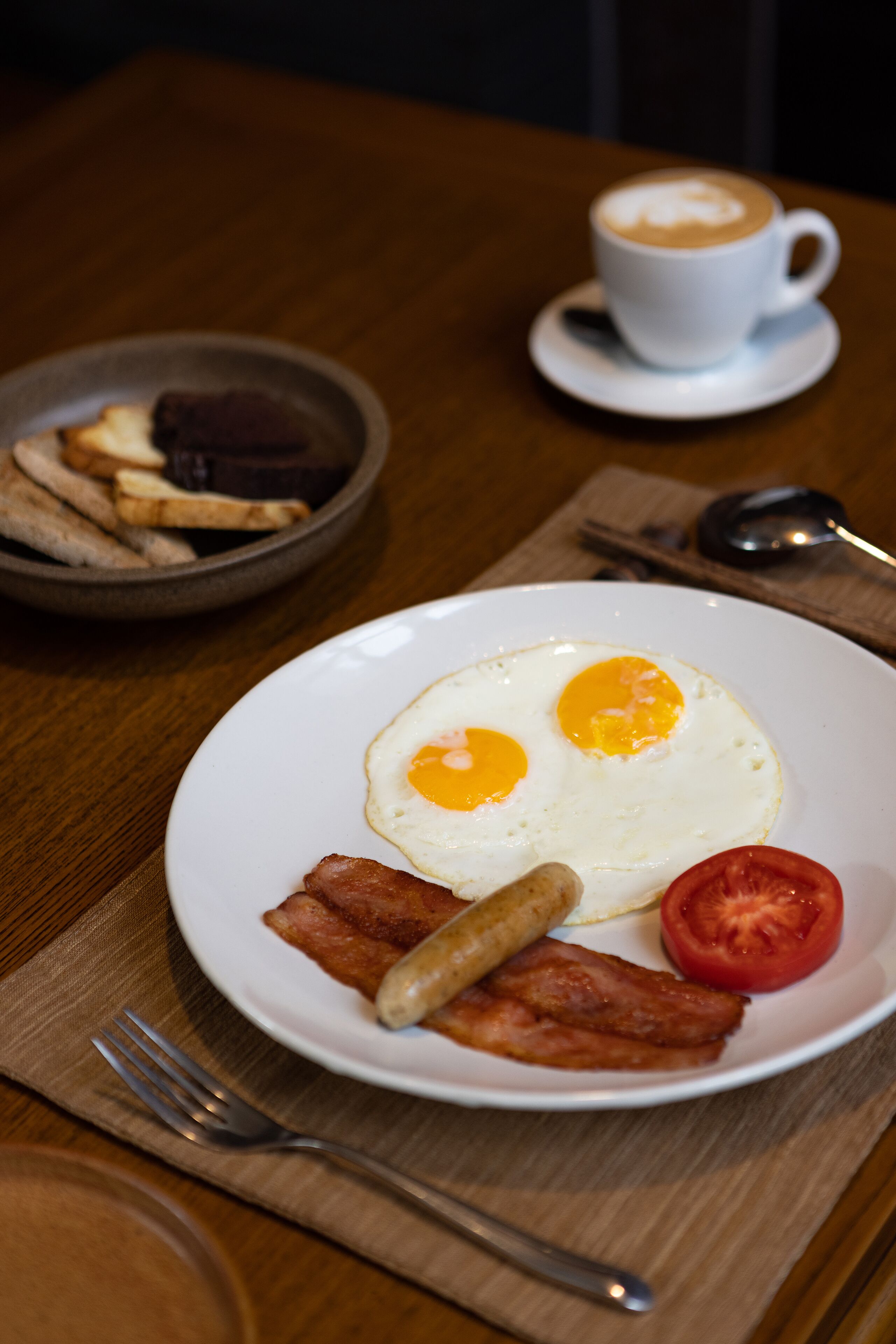 Un plato de desayuno con huevos, tocino y tomate sobre una mesa de madera.