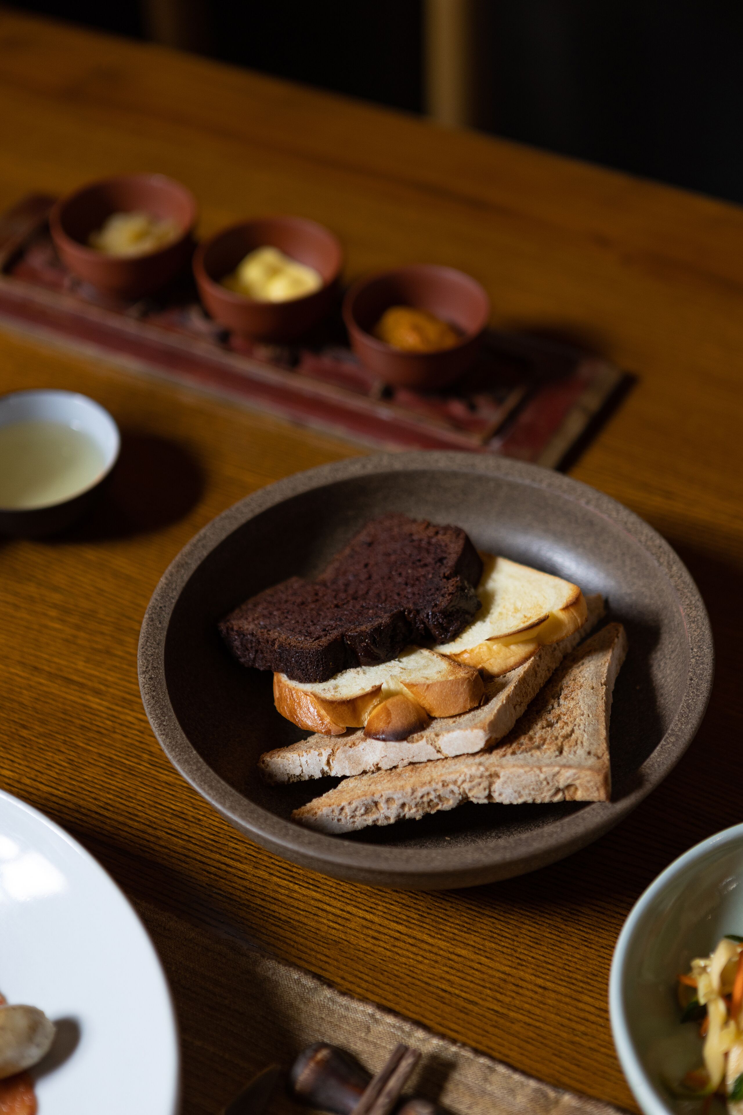 Una mesa de madera con un plato de pan y mantequilla, un tazón de sopa y un recipiente pequeño con nueces.