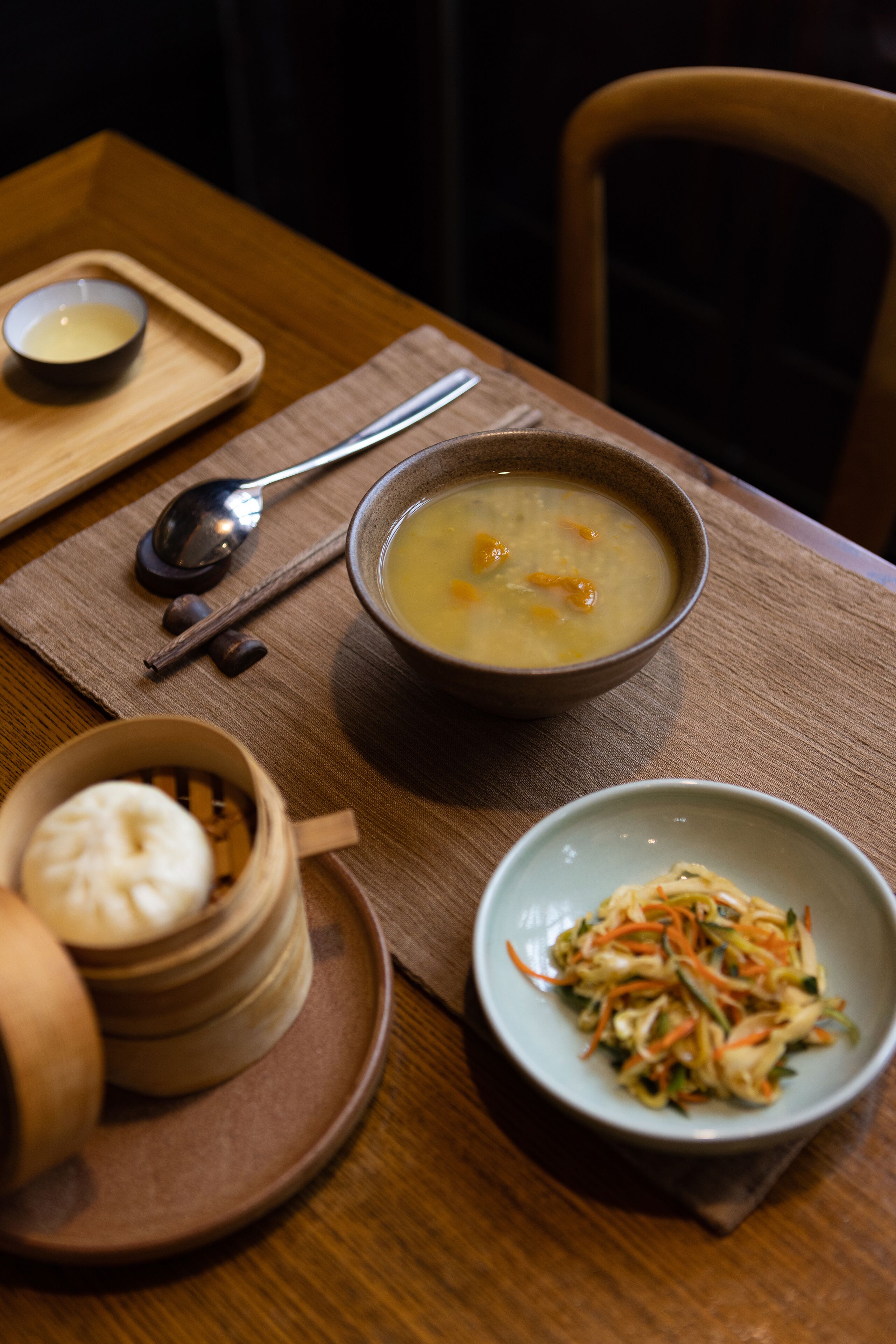 A dining table with a bowl of soup, a plate of vegetables, and a small bowl of dumplings.