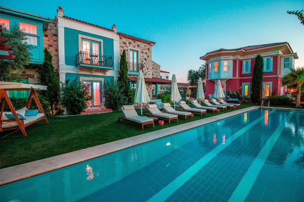 A swimming pool with lounge chairs and umbrellas, surrounded by colorful buildings with stone and stucco exteriors.