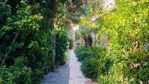 Ein gepflasterter Weg, gesäumt von üppigem Grün und farbenfrohen Blumen, führt zu einem Gebäude im traditionellen Baustil.