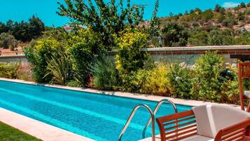 An outdoor dining area with a pool, wooden furniture, and a view of the landscape.