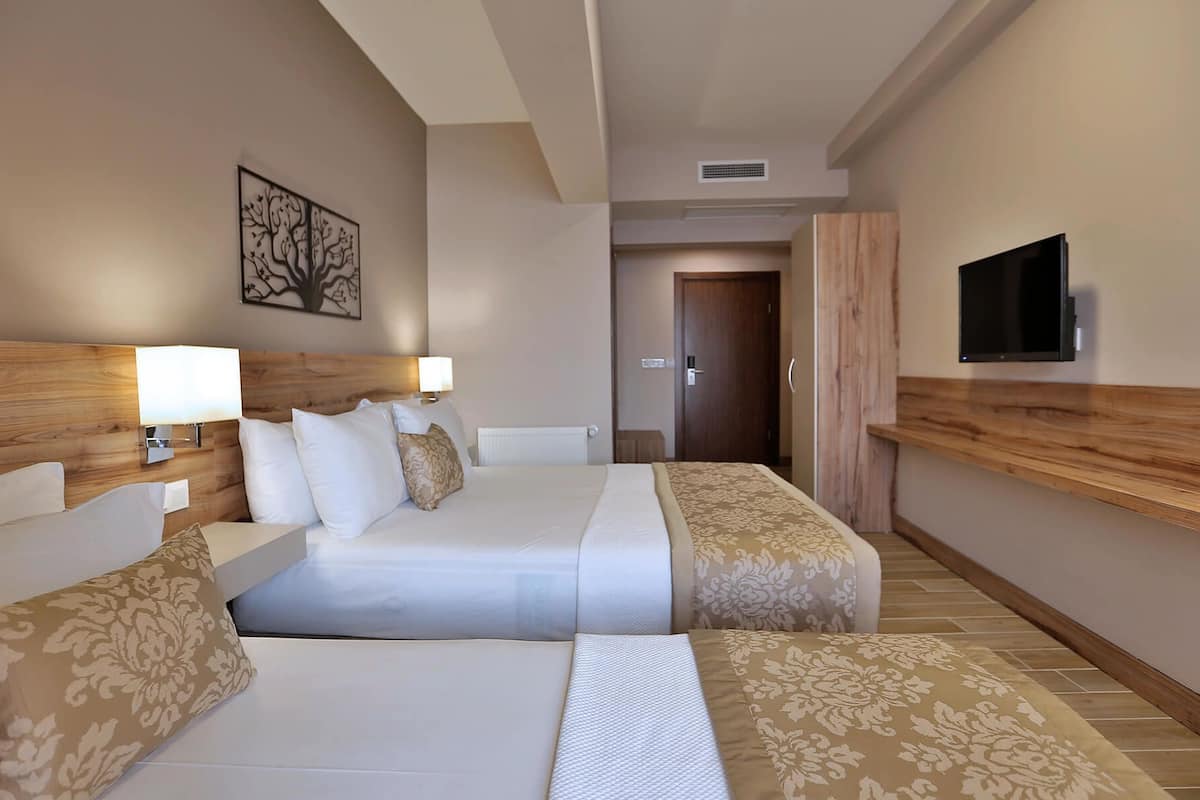 A hotel room with a double bed, a TV mounted on the wall, and a wooden headboard.