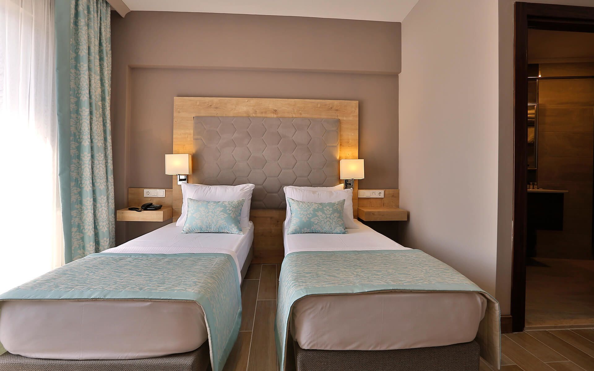 A hotel room with two beds, a wooden headboard, bedside lamps, and a nightstand with a phone.