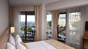 Une chambre d’hôtel avec un lit, une télévision et un balcon offrant une vue sur la mer et les bâtiments.