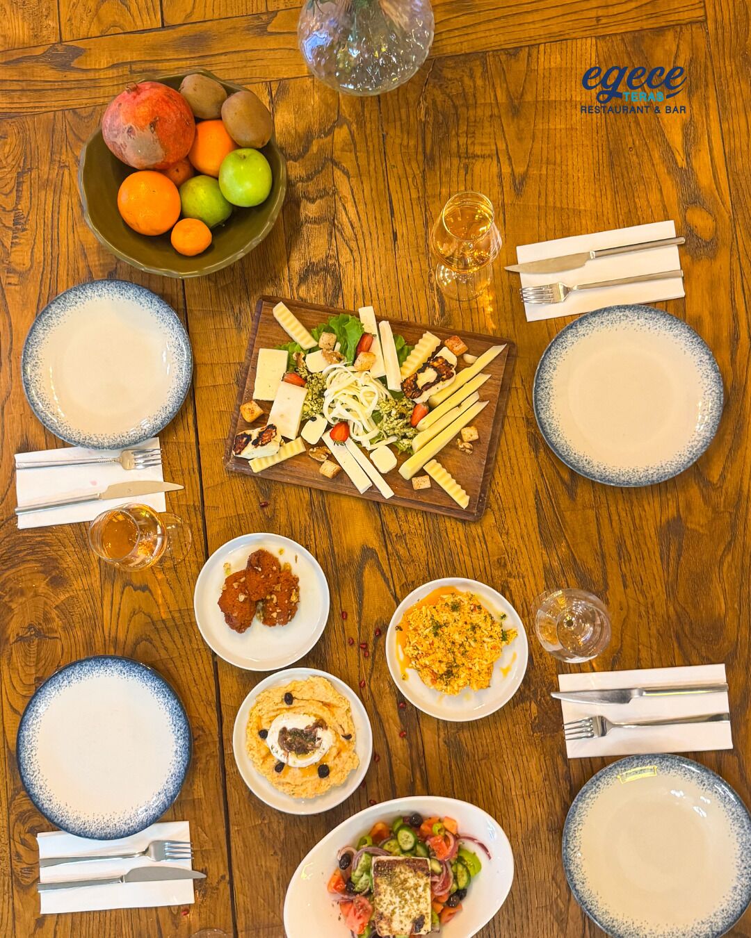 A wooden table with a variety of dishes, including a charcuterie board, salads, and a bowl of fruits.