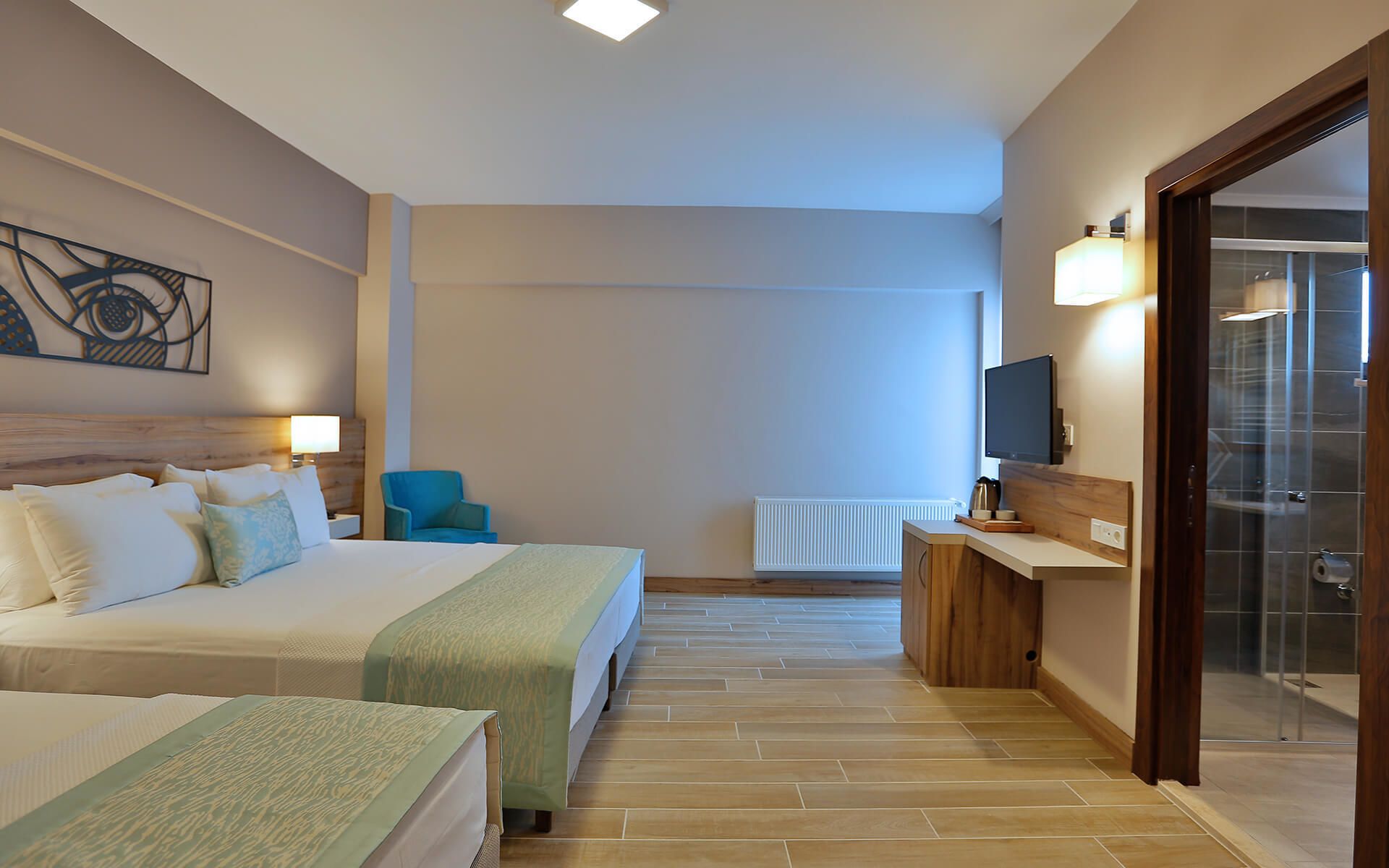 Une chambre d’hôtel avec deux lits, un bureau avec un ordinateur, une chaise, une télévision et une salle de bain visible à travers une porte en verre.