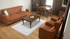 A living room with a sofa, coffee table, and armchairs, a dining table with chairs, a cabinet, and a TV. - Zarha Mountain Resort (Surmene)
