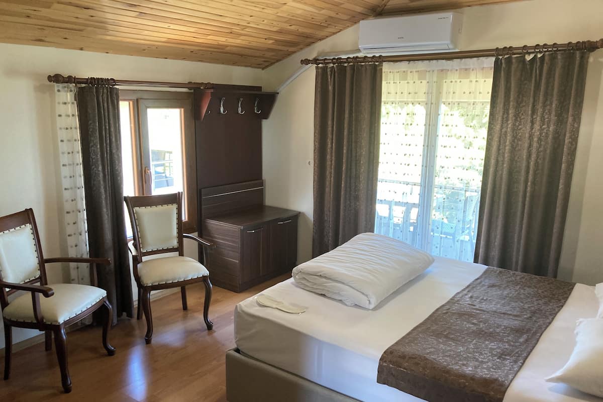 A bedroom with a bed, two chairs, a small desk, and a window with curtains.