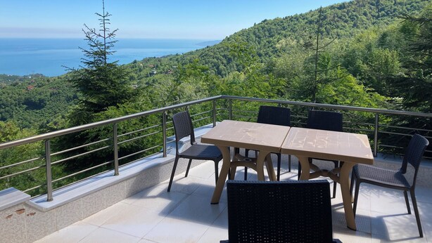 A balcony with a table and chairs, overlooking a lush green landscape and the sea. - Zarha Mountain Resort (Surmene)
