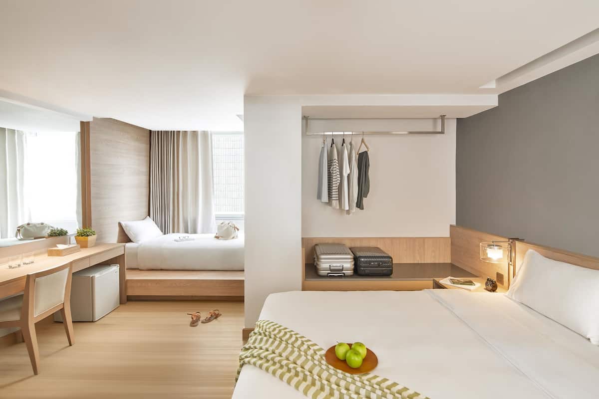 A hotel room with a bed, a desk, a chair, a small table, a lamp, and a window with curtains.