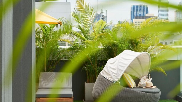 A rooftop garden with a seating area, green plants, and a cityscape view. - KritThai Residence (Bangkok)