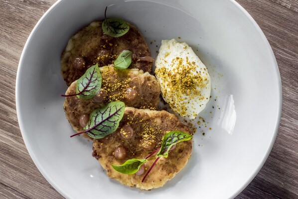 A white plate with food items including a poached egg, a piece of meat, and a flatbread, garnished with herbs and spices. - Hampton by Hilton Lublin (Lublin)
