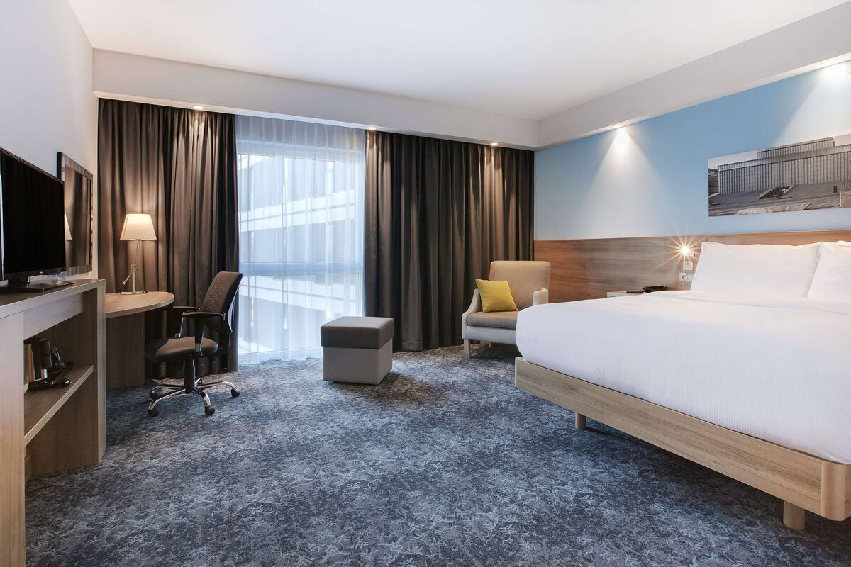 Une chambre d’hôtel comprenant un lit, un bureau avec un ordinateur, une chaise, un petit pouf et un téléviseur.