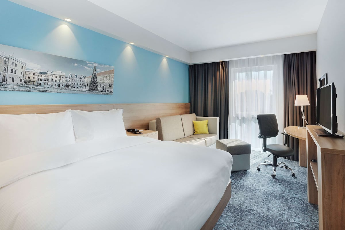 Une chambre d’hôtel avec un grand lit, un canapé, un bureau avec un ordinateur et une télévision.