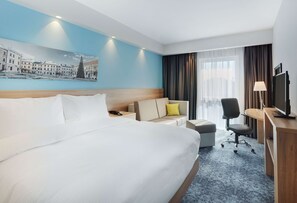 A hotel room with a large bed, a sofa, a desk with a computer, and a TV. - Hampton by Hilton Lublin (Lublin)