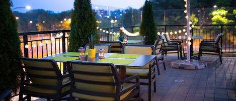 An outdoor patio with tables and chairs, a large umbrella, and string lights.