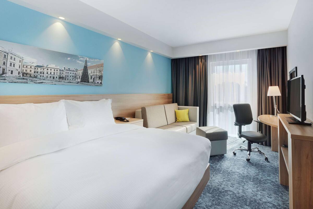 Une chambre d’hôtel avec un grand lit, un bureau, une chaise, un canapé et un téléviseur.