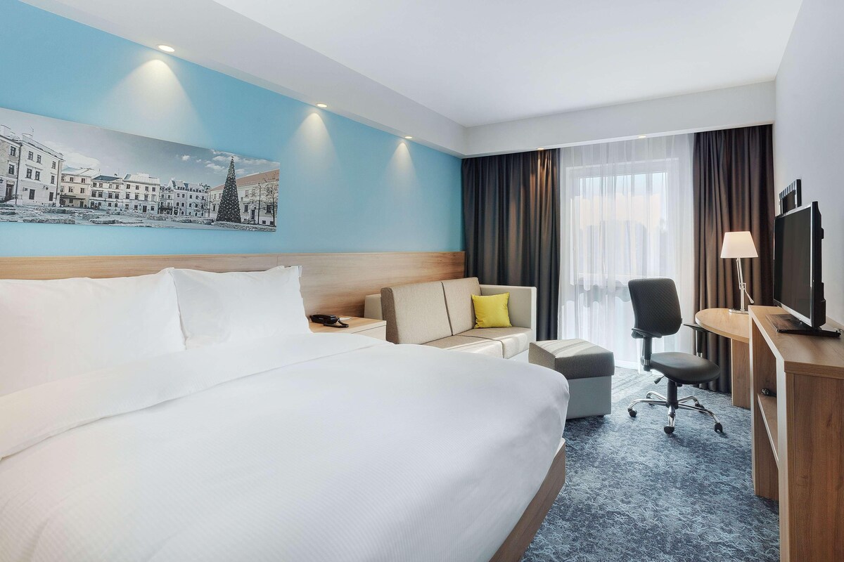 Habitación de hotel con una cama grande, un escritorio, una silla, un sofá y un televisor.