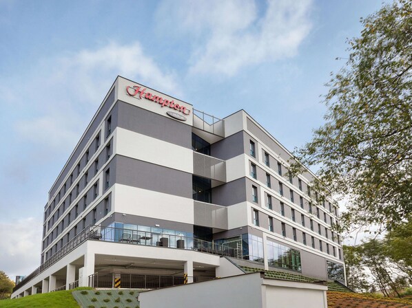 A modern hotel with a prominent Hilton logo, multiple floors, and a covered outdoor area with seating. - Hampton by Hilton Lublin (Lublin)