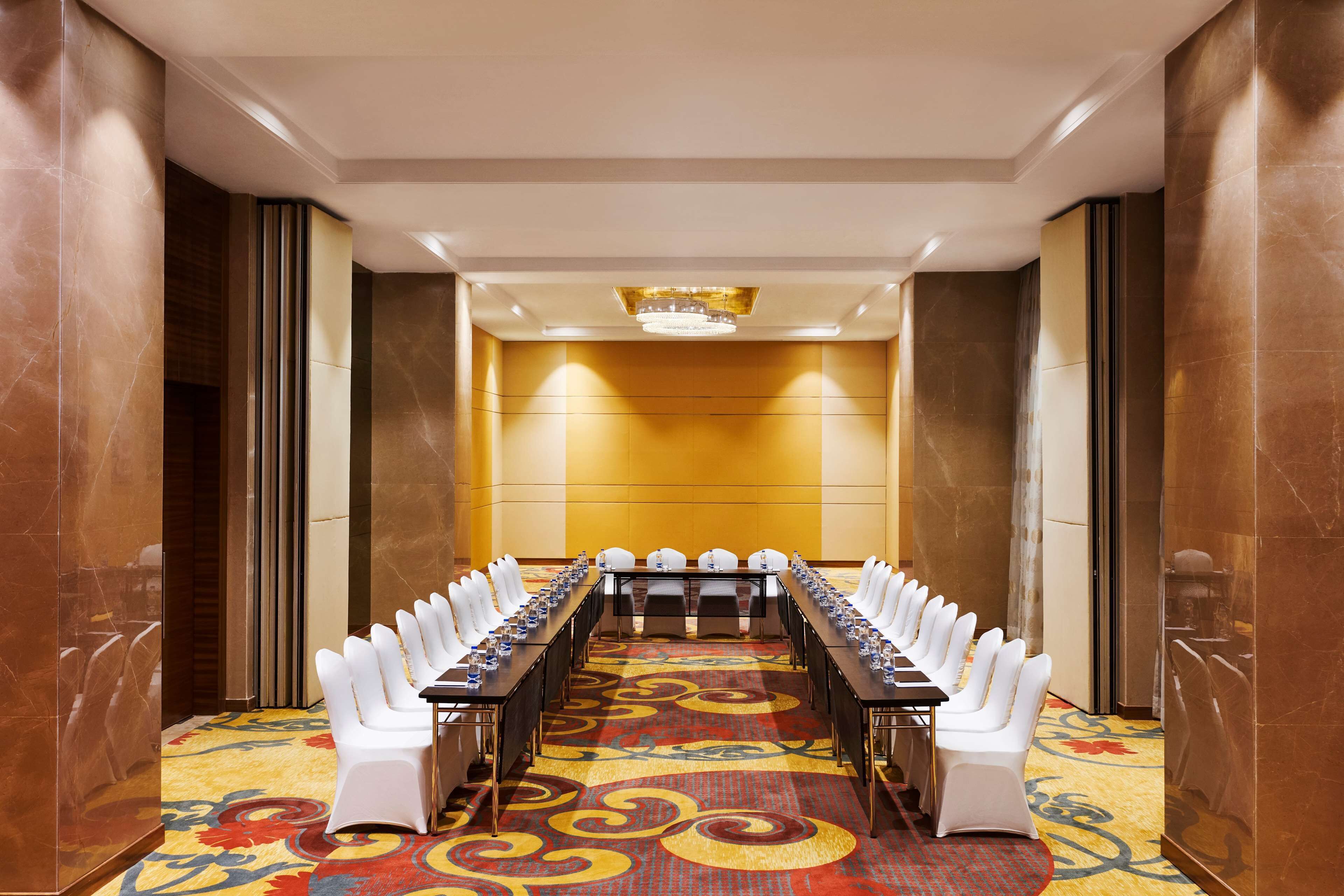 A conference room with a long table, white chairs, and a patterned carpet.