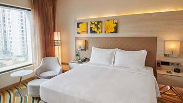 Ein Hotelzimmer mit einem großen Bett, einem kleinen runden Tisch, einem Sessel, einem Nachttisch mit Lampe und Bildern an der Wand.