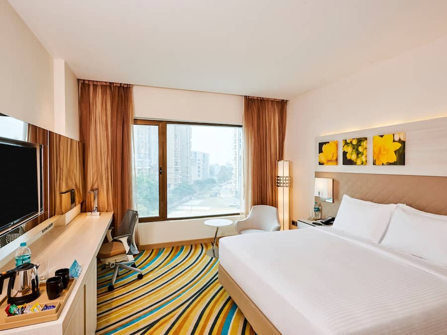 Habitación de hotel con una cama grande, un escritorio con televisión de pantalla plana, una mesita redonda pequeña, una silla y una ventana con cortinas.