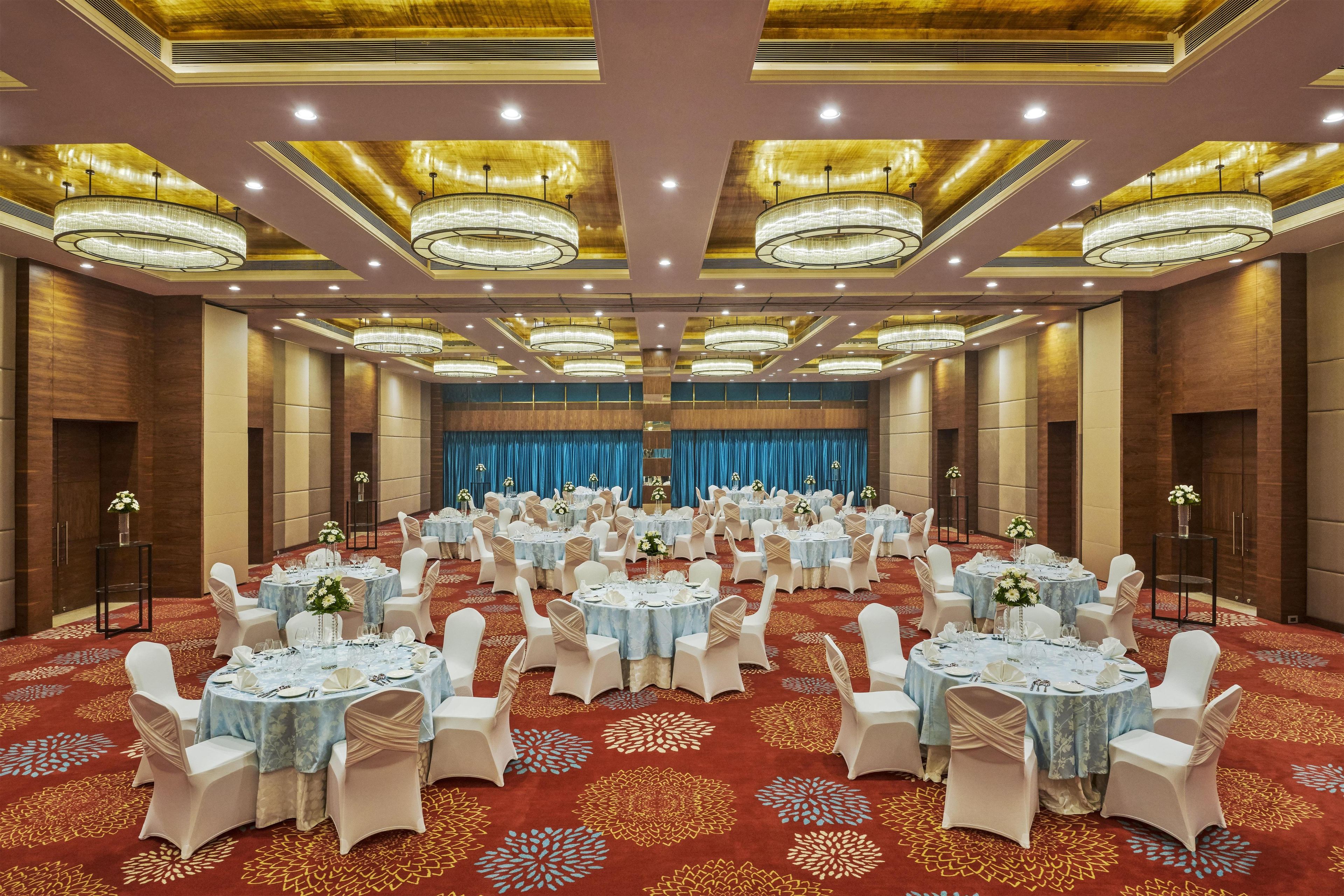 A banquet hall with round tables, white chairs, and chandeliers.