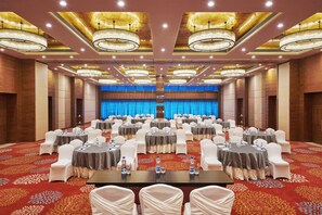 A large conference room with round tables, white chairs, and chandeliers.