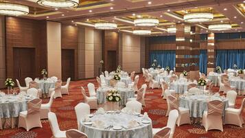A banquet hall with round tables, white chairs, and floral centerpieces.