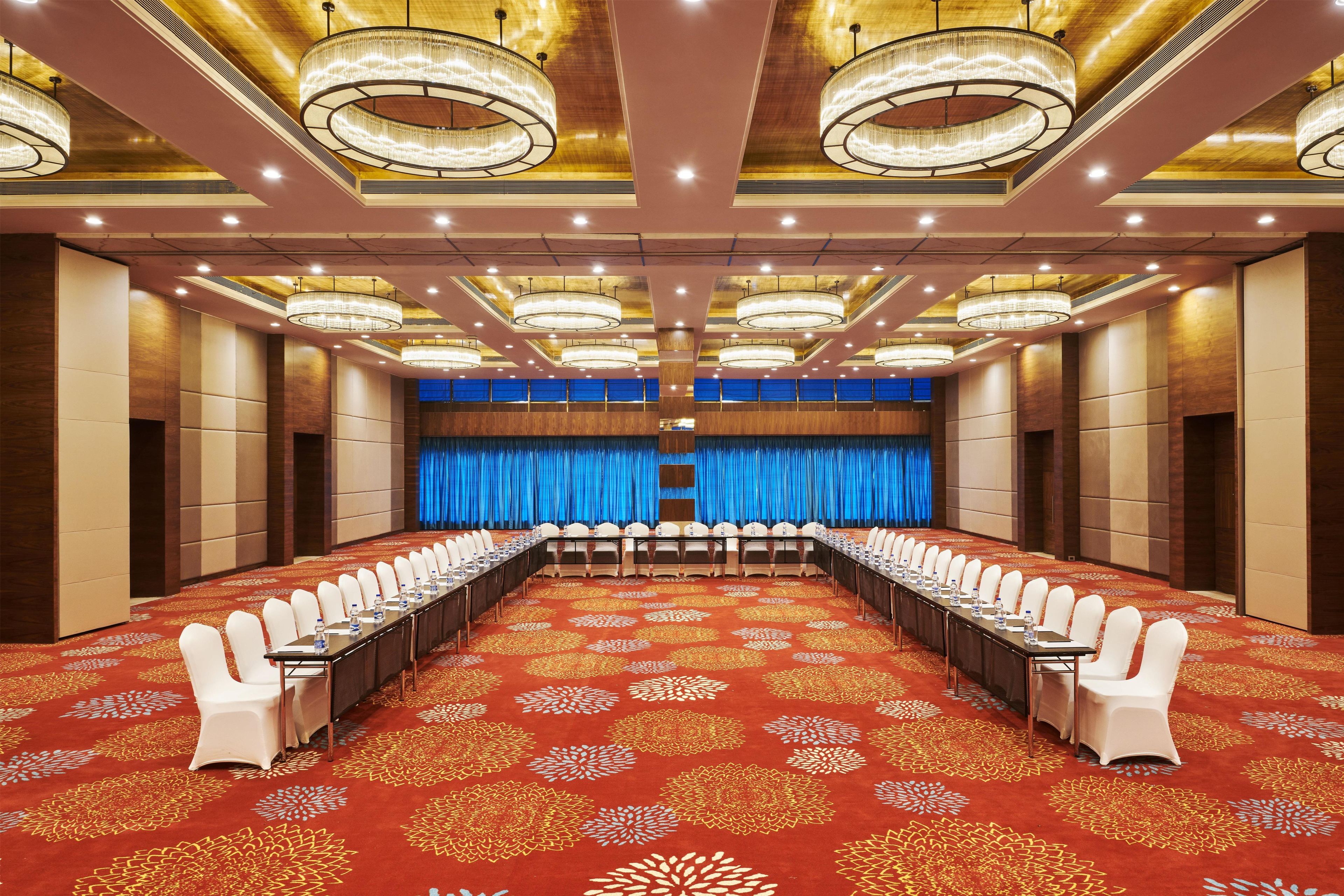 A conference room with a long table, white chairs, and a red carpet with floral patterns.