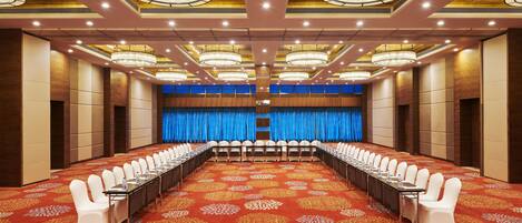A conference room with a long table, white chairs, and a red carpet with floral patterns.