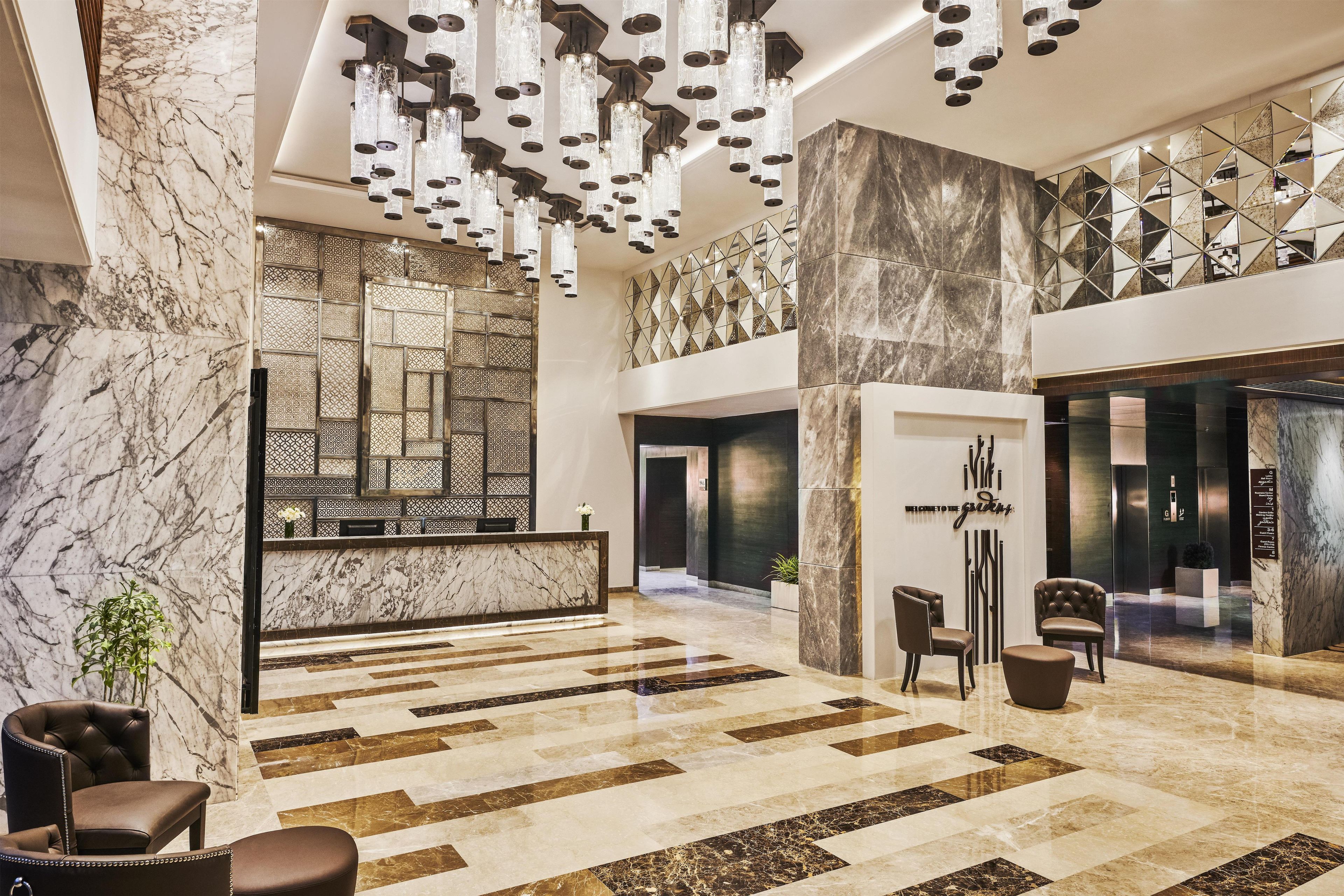 A spacious lobby with a marble reception desk, modern lighting fixtures, and a geometric wall design.