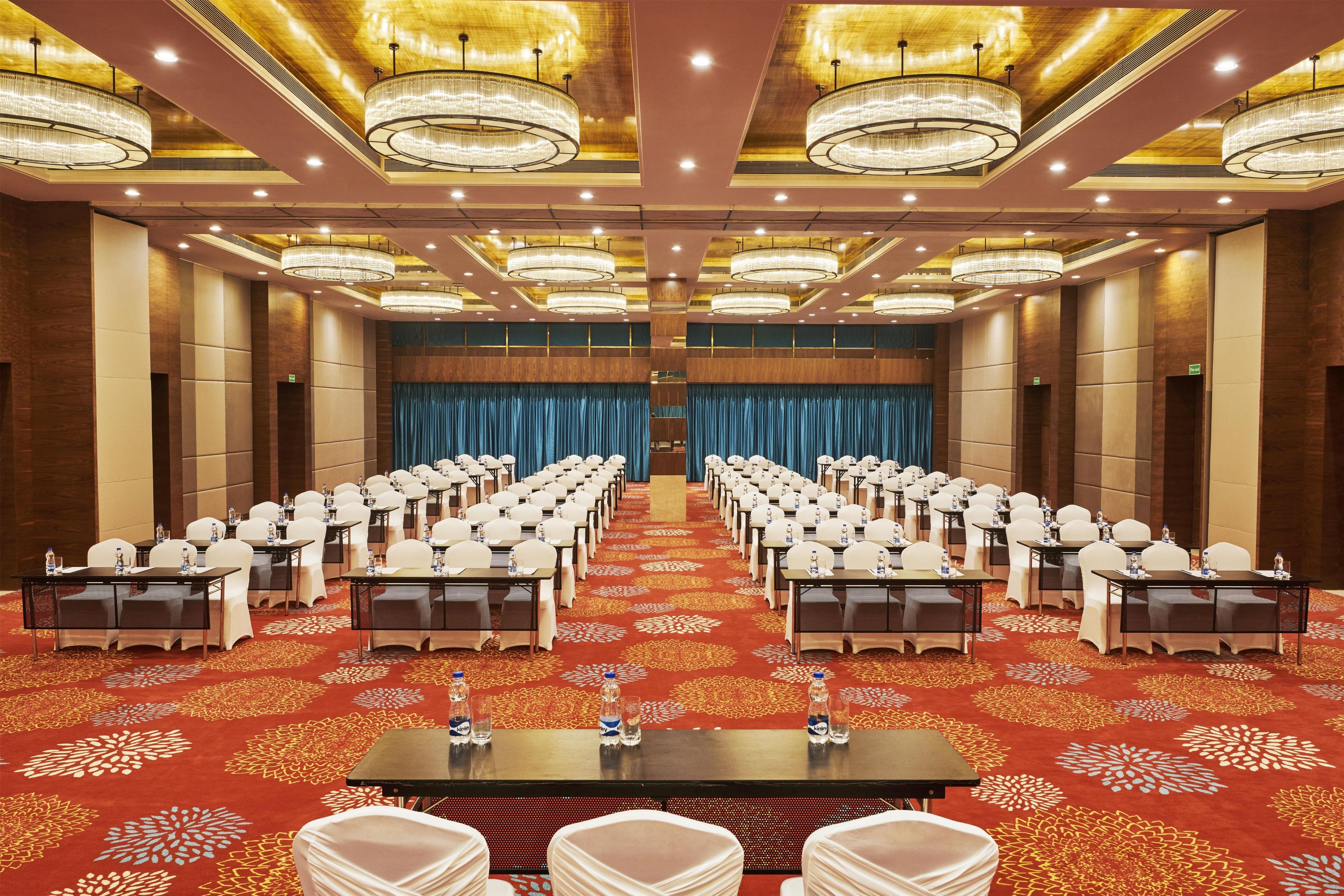 A conference room with rows of tables and chairs, a patterned carpet, and a large chandelier.