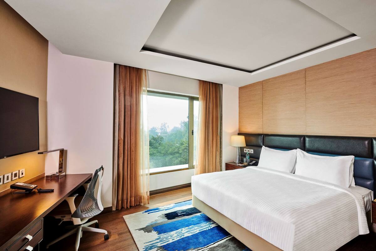 A hotel room with a bed, desk, chair, TV, and a window with curtains.