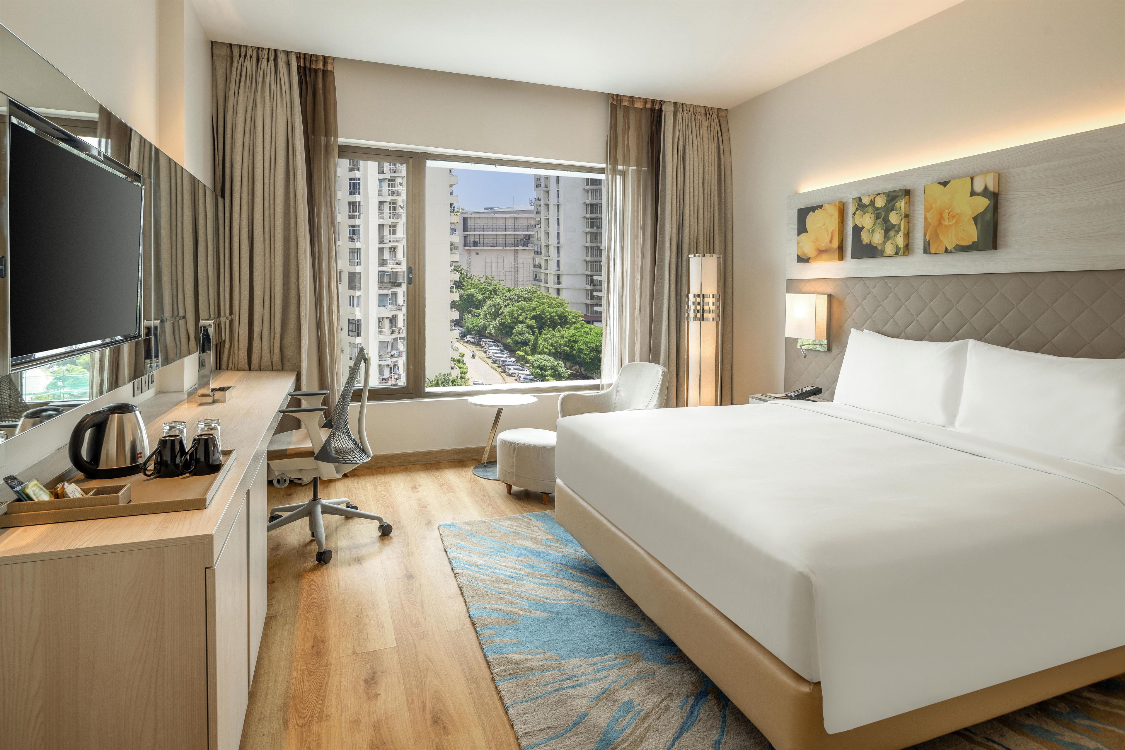Une chambre d’hôtel équipée d’un lit, d’un bureau, d’une chaise et offrant une vue sur la ville par la fenêtre.